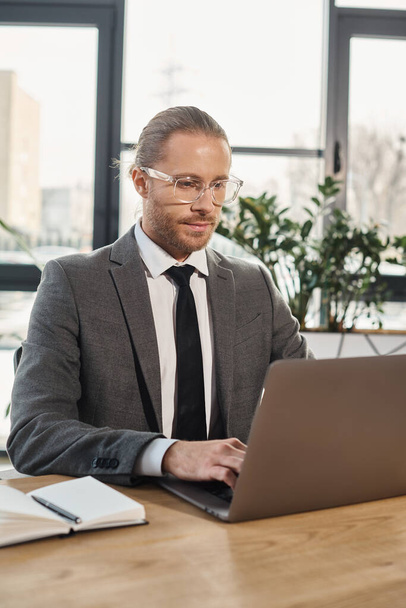 skoncentrowany przedsiębiorca w okularach i formalnym ubraniu pracujący na laptopie w nowoczesnej przestrzeni biurowej - Zdjęcie, obraz
