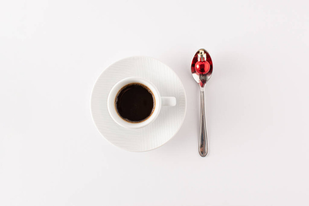 Cup of coffee and spooh with red Christmas decoration ball isolated on white background. Minimal Christmas morning coffee concept. Copy space. Flat lay. - Photo, Image