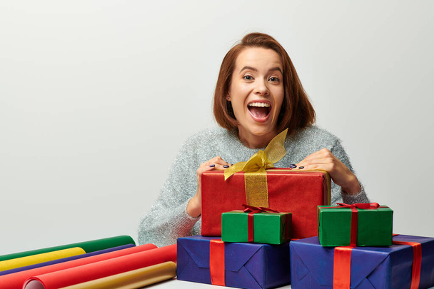 Kış süveteri içinde hayretler içinde bir kadın hediye paketi ve gri, Noel üzerine renkli bir hediye kağıdı. - Fotoğraf, Görsel