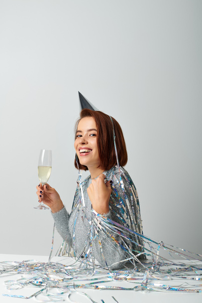 radosna kobieta w czepku imprezowym z błyskotką na głowie trzymająca kieliszek szampana podczas świąt Bożego Narodzenia - Zdjęcie, obraz