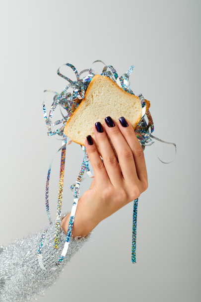 cropped female hand holding sandwich with shiny tinsel on grey backdrop, Happy New Year concept - Photo, Image