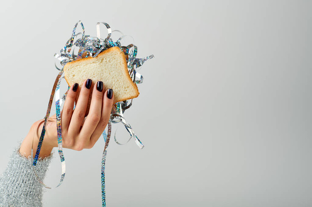 Gri arka planda parlak süslemeli sandviç tutan bir kadın görüntüsü. Mutlu yıllar konsepti. - Fotoğraf, Görsel