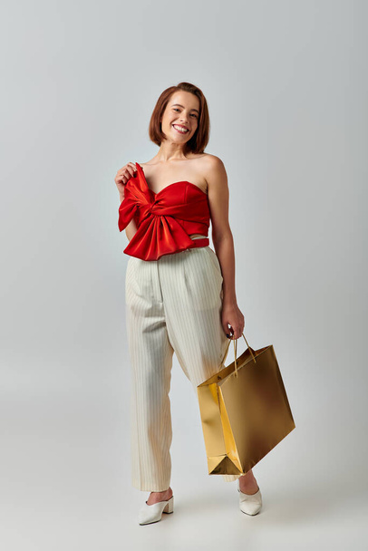 Compras de Navidad, mujer joven feliz en traje de moda caminando con bolsa de compras sobre fondo gris - Foto, Imagen