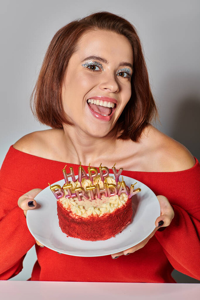 beschnitten glückliche Frau in roter Kleidung in der Nähe bento Kuchen mit Happy Birthday Kerzen auf grauem Hintergrund - Foto, Bild