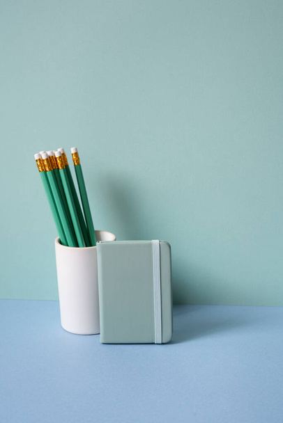 Bleistifthalter und Tagebuchheft auf blauem Schreibtisch. mintgrüner Hintergrund - Foto, Bild