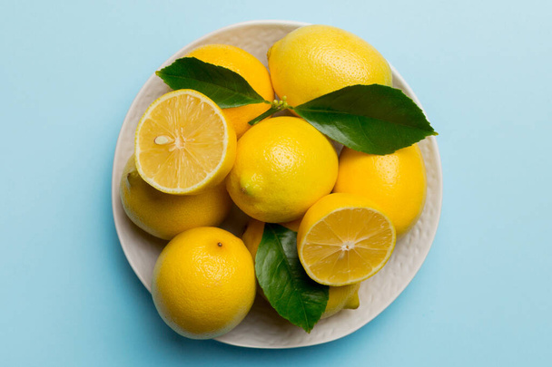 新鮮なレモンと丸皿の上のレモン全体を色の背景にカットしました。食べ物や飲み物の成分を準備。健康的な食事のテーマコピースペースでトップビュー. - 写真・画像