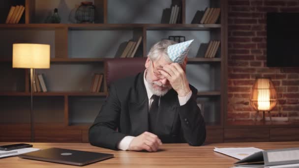 Employé âgé fatigué avec chapeau de cône d'anniversaire sur la tête se détendre après une dure journée de travail au bureau. Gestionnaire professionnel fatigué de prendre une pause des célébrations d'entreprise dans le confort de la salle de réunion calme. - Séquence, vidéo