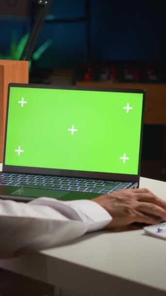 Verticale video Arabische man scrollen op mockup laptop tijdens het werken vanuit huis. Zelfstandige die e-mails schrijft op geïsoleerd schermapparaat in appartementenkantoor met TV als achtergrondgeluid - Video