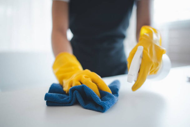 Sprzątanie powierzchni biurka w biurze sprayem do dezynfekcji, noszenie rękawiczek i wycieranie stołu ręcznikiem, gospodyni sprząta biurko dla higieny z powodu Covid-19, pomysł czyszczenia. - Zdjęcie, obraz