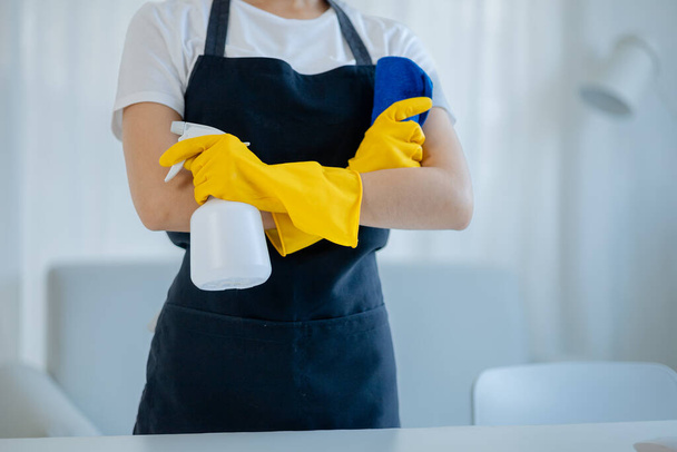 Азиатские женщины носят униформу, чтобы подготовиться к работе по дому, носить фартук и резиновые перчатки, чтобы защитить от чистки химических веществ, экономка улыбается счастливо, прежде чем начать работу, уборка идея. - Фото, изображение