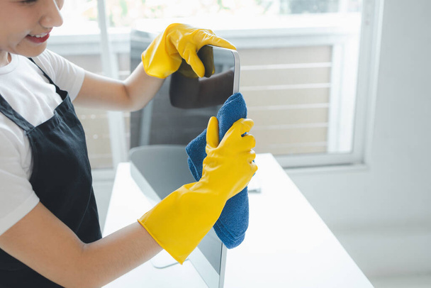 Asian female cleaner, Wear rubber gloves and an apron and work with a happy smile, Cleaning staff wiping down office equipment, Wipe the monitor clean with a towel and sanitizer, cleaning idea. - Photo, Image