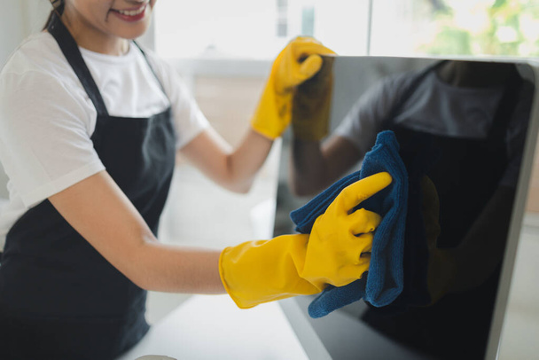Asian female cleaner, Wear rubber gloves and an apron and work with a happy smile, Cleaning staff wiping down office equipment, Wipe the monitor clean with a towel and sanitizer, cleaning idea. - Photo, Image