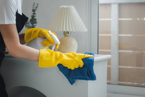 Evdeki mobilyaları temizleyen temizlikçi, temizlik kimyasallarına karşı önlük ve lastik eldiven takan, masaları temizleyen, temizlik spreyiyle temizleyen bir kadın.. - Fotoğraf, Görsel