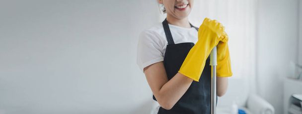 Asijské ženy nosí uniformy pro přípravu na úklid práce, nosit zástěru a gumové rukavice na ochranu proti čištění chemikálií, hospodyně se šťastně usmívá před zahájením práce, úklid nápad - Fotografie, Obrázek