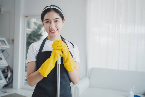Aasialaiset naiset käyttävät univormuja valmistellakseen kodinhoitotyötä, käyttävät esiliinaa ja kumihanskoja kemikaalien puhdistamiseksi, taloudenhoitaja hymyilee iloisesti ennen työn aloittamista, puhdistusainetta. - Valokuva, kuva