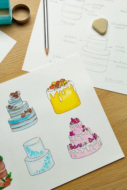 Ο ζαχαροπλάστης αναπτύσσει ένα σχέδιο κέικ ζωγραφίζοντας σε χαρτί. Δημιουργία προϊόντων ζαχαροπλαστικής. - Φωτογραφία, εικόνα