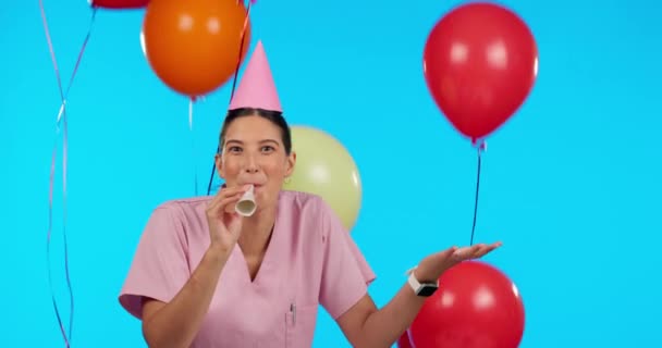 Geburtstag, Party-Hupe und Luftballons mit einer Krankenschwester im Studio isoliert auf blauem Grund zum Feiern. Porträt, Gesundheitswesen und eine glückliche Medizinerin, die auf einen Krachmacher weht. - Filmmaterial, Video