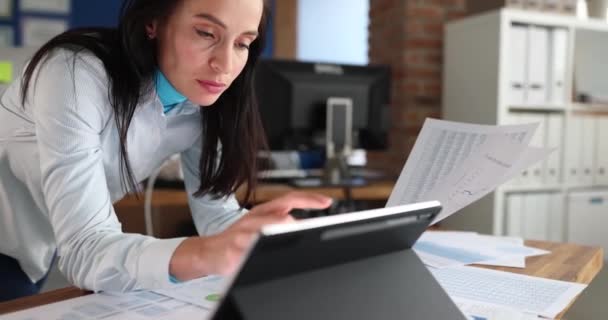 Femme regardant dans la tablette numérique avec des documents avec des graphiques dans les mains au bureau tard dans la nuit film 4k ralenti. Date limite dans le concept d'entreprise - Séquence, vidéo
