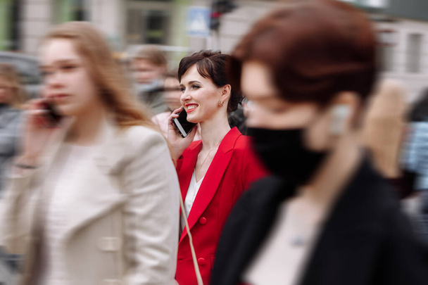 Eine junge selbstbewusste Geschäftsfrau in Formalbekleidung, roter Jacke spricht auf einem Spaziergang durch die Stadt mit dem Smartphone. Telekommunikation und mobiles Netzwerk für Geschäftskonzept. Weiblicher Geschäftsstil. - Foto, Bild