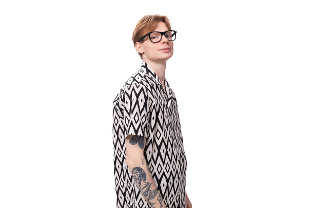 a young stylish man with red hair and a tattoo on his arms is dressed in a short-sleeve shirt with a diamond pattern. - Photo, Image