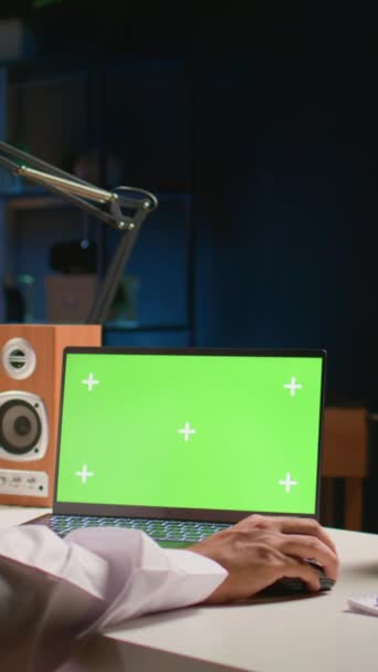 Вертикальне відео Мусульманський чоловік прокручує на зеленому екрані ноутбук, перевіряючи стрічку соціальних мереж. Самозайнята людина, яка серфінгує в Інтернеті з ключового пристрою хромосоми в багатоквартирному офісі з телевізором як фоновий шум - Кадри, відео