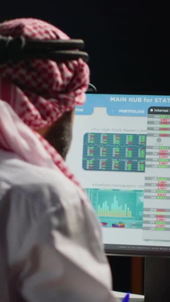 Вертикальне відео Арабський брокер інвестор у темній квартирі перевіряє оцінку фондової біржі, записуючи цифри фінансового прибутку. Близькосхідний телевізійний акціонер бізнесмен дивиться на ринок - Кадри, відео