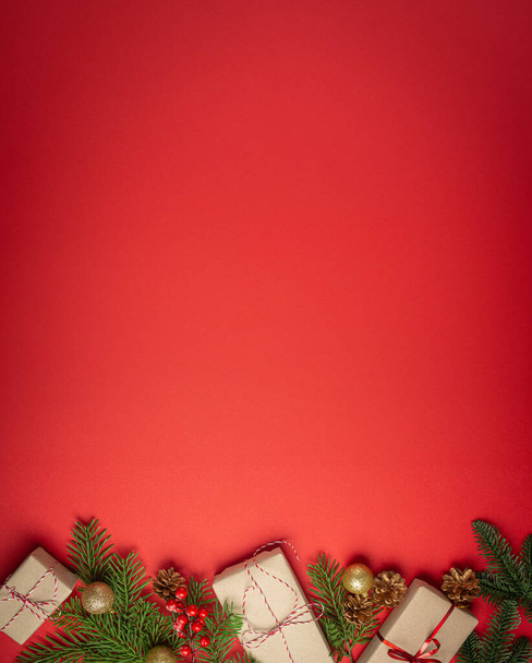 Christmas or New Year celebration red paper festive background with decoration fir tree, wrapped present boxes, cones, berries, sparkly red balls. Space for text.. - Photo, Image