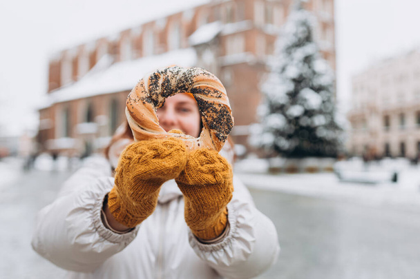 Attrayant jeune touriste féminine au chapeau jaune tient bretzel, bagel polonais traditionnel sur la place du marché à Cracovie. Voyager en Europe en hiver. - Photo, image
