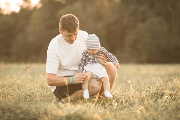 Ένας μπαμπάς απολαμβάνει μια παιχνιδιάρικη στιγμή σε ένα καλοκαιρινό χωράφι, καθώς ο μπαμπάς πετάει τον μικρό γιο του. Η χαρούμενη οικογένεια κοιτάζει με χαρά και αγάπη - Φωτογραφία, εικόνα