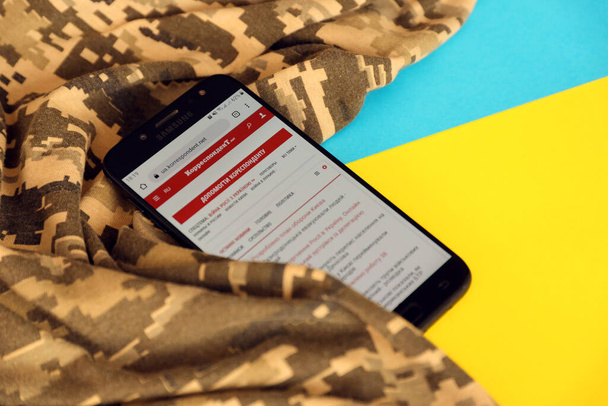 КИЕВ, Украина - 4 мая 2023 года: Корреспондент украинского новостного портала на экране смартфона с украинским флагом и камуфляжной тканью крупным планом - Фото, изображение