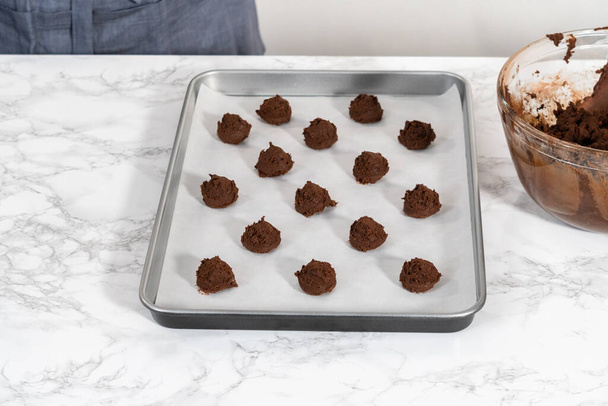 Scooping cookie dough with dough scoop into a baking sheet lined with parchment paper to bake chocolate cookies with chocolate hearts for Valentines Day. - Fotó, kép