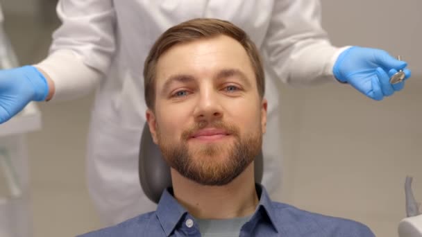 Portret van een gelukkige man zittend aan een tandartsstoel in een moderne kliniek en lachend. Patiënt die tandheelkundige behandeling met professionele tandarts geniet - Video