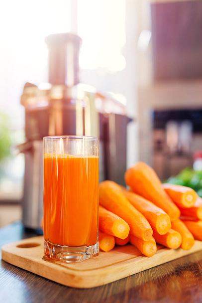 Bicchiere di succo di carota appena spremuto, carote e spremiagrumi in cucina. Stile di vita sano concetto - Foto, immagini