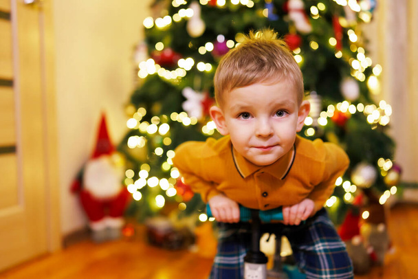 Menino feliz sentado na bicicleta empurrar em um fundo de árvore de Natal. Véspera de Natal - Foto, Imagem