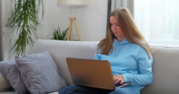 Jovem mulher sentada no sofá usando laptop olhando a mensagem de digitação de tela, mulher conversando no computador, navegando na internet mídia social estudando ou trabalhando on-line em casa - Filmagem, Vídeo