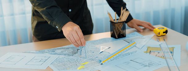 A portrait of architect using divider to measure blueprint. Architect designing house construction on a table at studio, with architectural equipment scattered around. Focus on hand. Delineation - Photo, Image