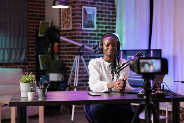 Afrykański Vlogger nagrywający program internetowy przy użyciu nowoczesnej kamery, mówiący o tematach historycznych. Influencer filmowanie transmisji na żywo za pomocą profesjonalnych urządzeń w salonie studio - Zdjęcie, obraz
