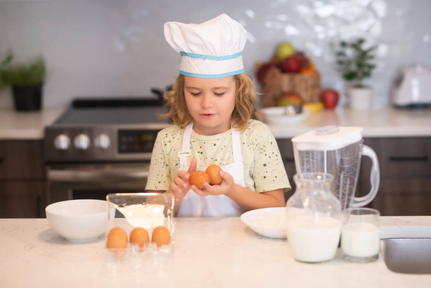 Kinderkoch kochen mit Eiern. Lustige kleine Kinderkoch mit einheitlichen Kochmütze und Schürze kochte Essen in der Küche. Kinder bereiten Teig zu, backen Plätzchen in der Küche - Foto, Bild