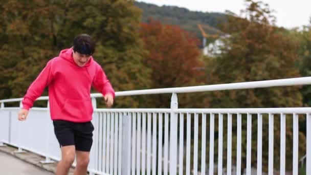 Läufer in farbigen Kleidern überqueren morgens die Brücke. Der Athlet ist des Laufens müde. Hochwertiges 4k Filmmaterial - Filmmaterial, Video