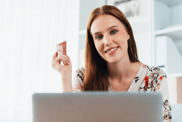Junge glückliche Frau kauft Produkt durch Online-Shopping zu Hause, während die Bestellung von Artikeln aus dem Internet mit Kreditkarte Online-Zahlungssystem durch äußerste Cyber-Sicherheit von Online-Shop-Plattform geschützt - Foto, Bild