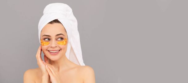 gelukkig meisje met badstof handdoek gebruik gezicht gouden ooglapje voor de huid, gezonde huid. Mooie vrouw geïsoleerde gezicht portret, banner met mock up kopieerruimte - Foto, afbeelding