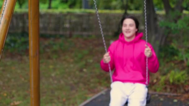 man in a pink jacket riding on a swing, rejoices and smiles, concept of a happy childhood. High quality 4k footage - Footage, Video