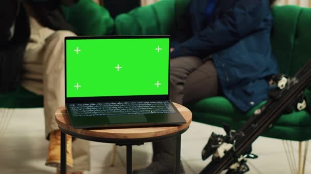 Digital device with greenscreen template placed on coffee table in lounge area at luxury alpine ski resort. People sitting on couch chatting, laptop running isolated copyspace display at hotel. - Footage, Video