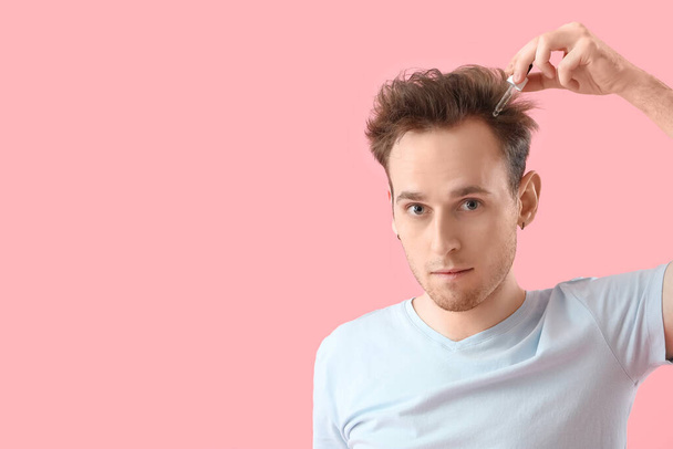 Hombre joven usando suero para el crecimiento del cabello sobre fondo rosa - Foto, Imagen