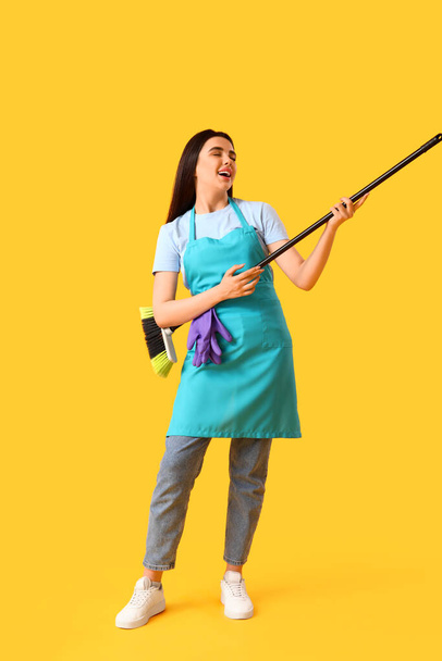 Female janitor with broom singing on yellow background - Photo, Image