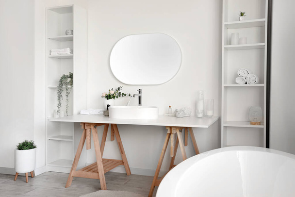 Interior de baño ligero con lavabo blanco, bañera y estanterías - Foto, imagen