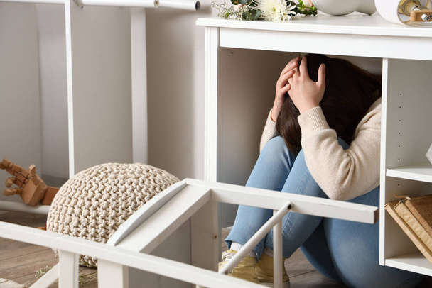 Junge Frau versteckt sich bei Erdbeben zu Hause unter Tisch - Foto, Bild