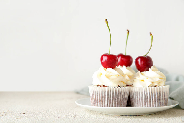 Piatto con gustosi cupcake di ciliegie su sfondo chiaro - Foto, immagini