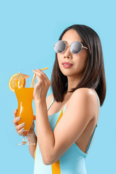 Krásná asijská žena v plavkách a s citrusovým koktejlem na modrém pozadí - Fotografie, Obrázek