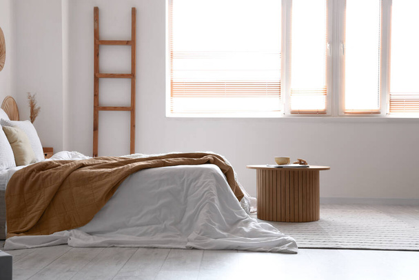 Acogedora cama con manta blanca y mesa de centro en el interior del dormitorio luminoso - Foto, Imagen
